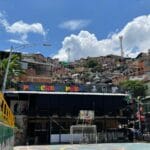 Panoramic view of Comuna 13 Medellín with brick houses and street life under a bright blue sky.