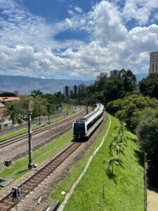 Medellín Metro train traveling through the city under a blue sky with mountains in the background