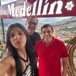 Turistas tomándose una selfie en un mirador con vista panorámica de Medellín, Colombia, junto al cartel de Medellín y flores decorativas.