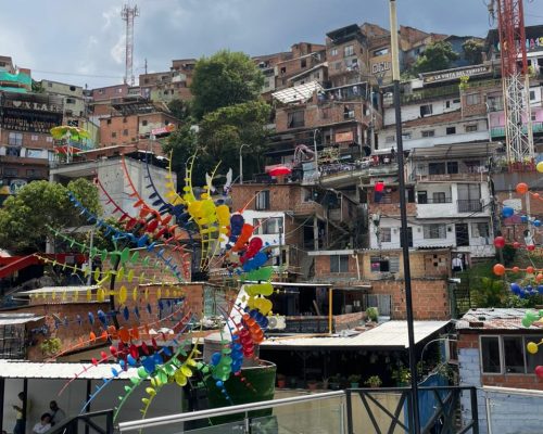 Panoramic view of Comuna 13 Medellín with colorful houses, street art, and a sculpture made of bright circular shapes, representing creativity and social transformation.